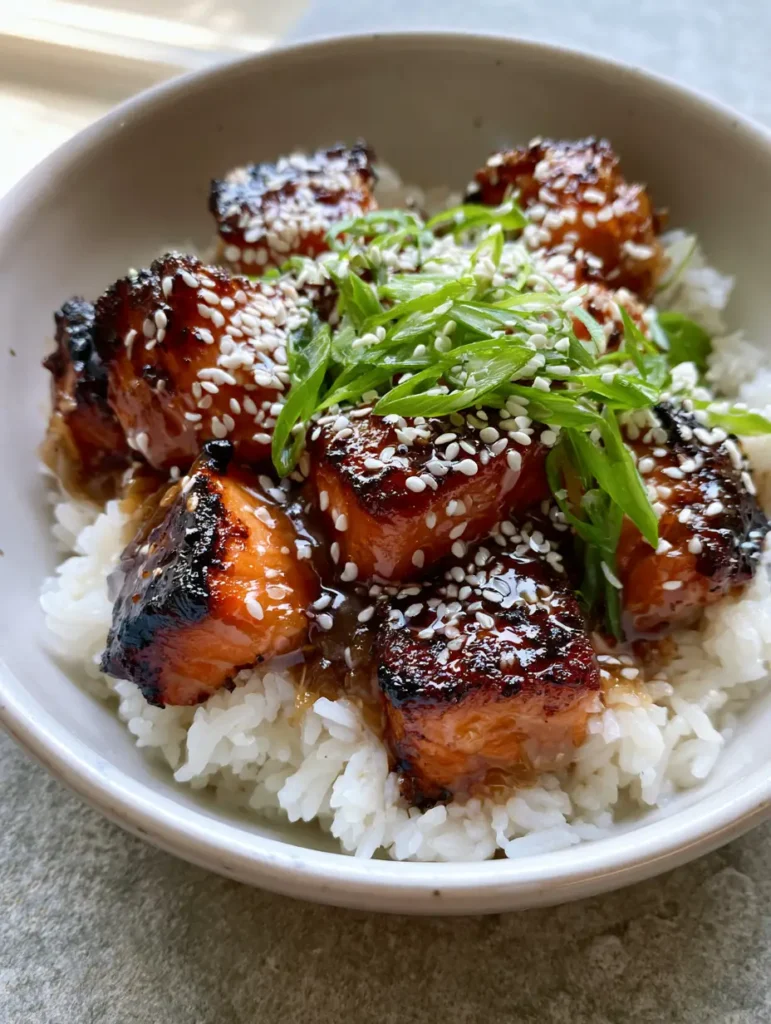 Detail shot of glossy, translucent amber honey garlic sauce coating crispy seared salmon bites.