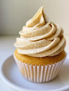 Close-up of thick tan frosting with dark toasted milk solid specks and matte finish. (Brown Butter Frosting Recipe)