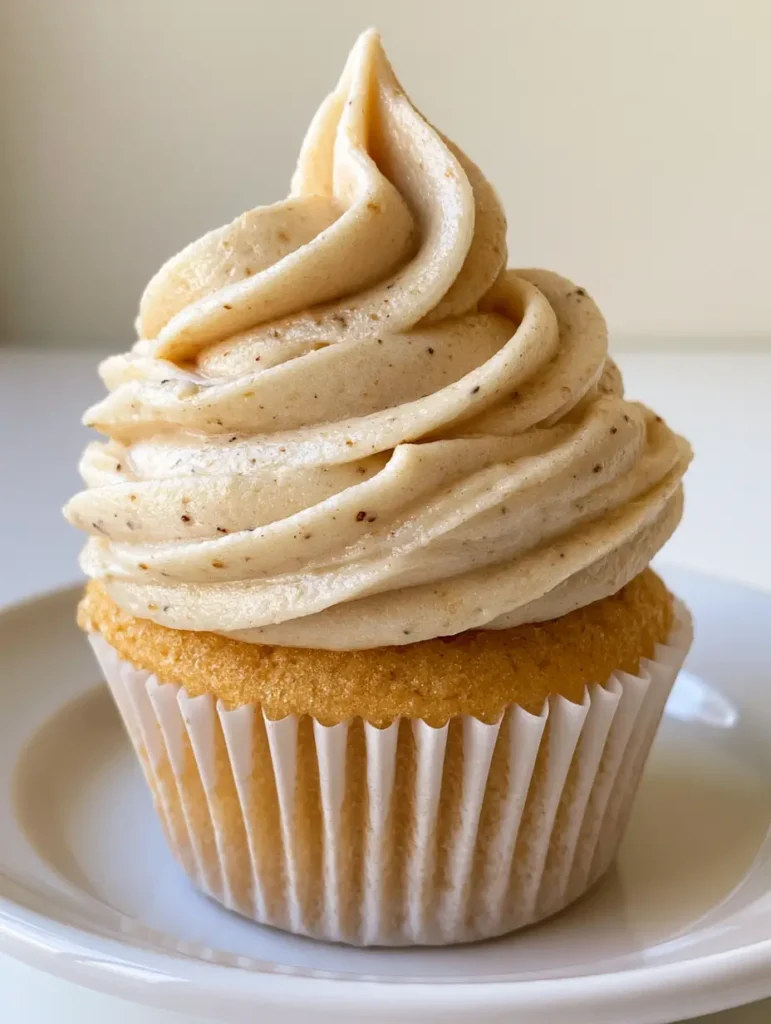 Moist golden vanilla cupcake topped with a tall brown butter frosting swirl on a white plate.