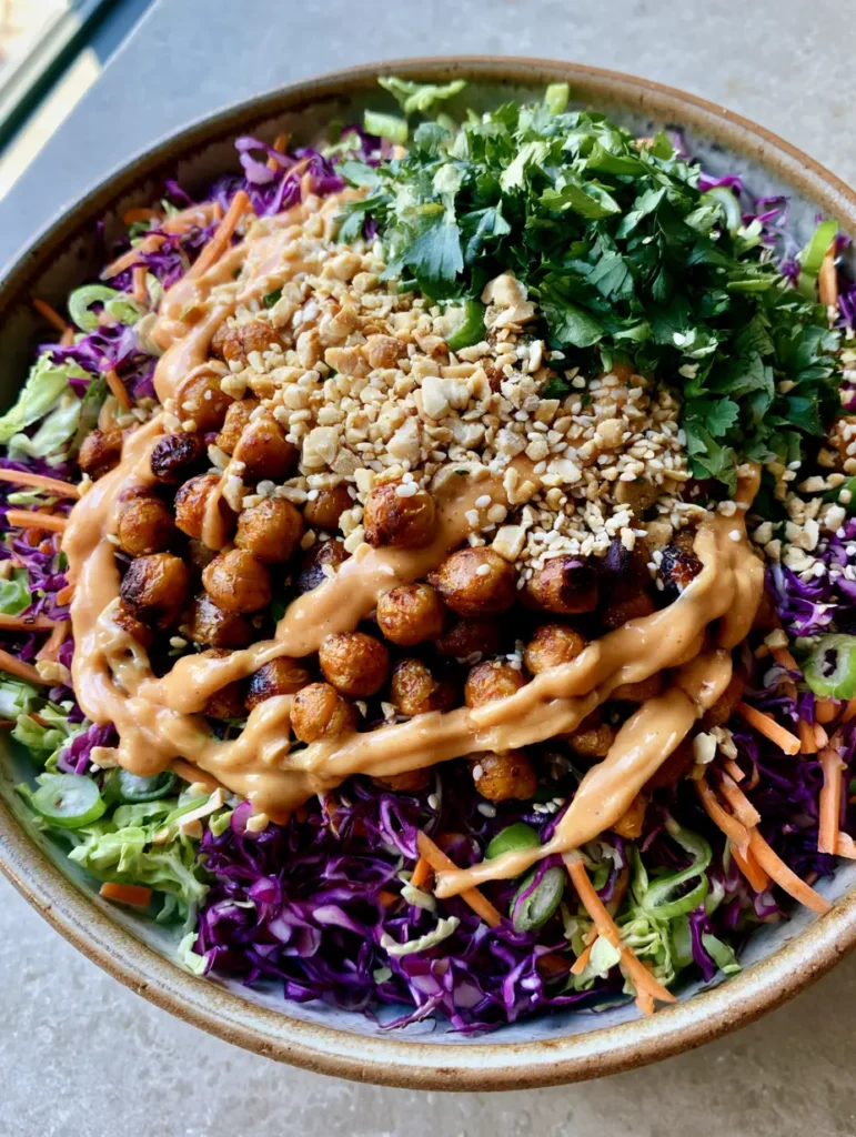 A rustic ceramic bowl filled with Crunchy Thai Chickpea Salad on a grey stone countertop.