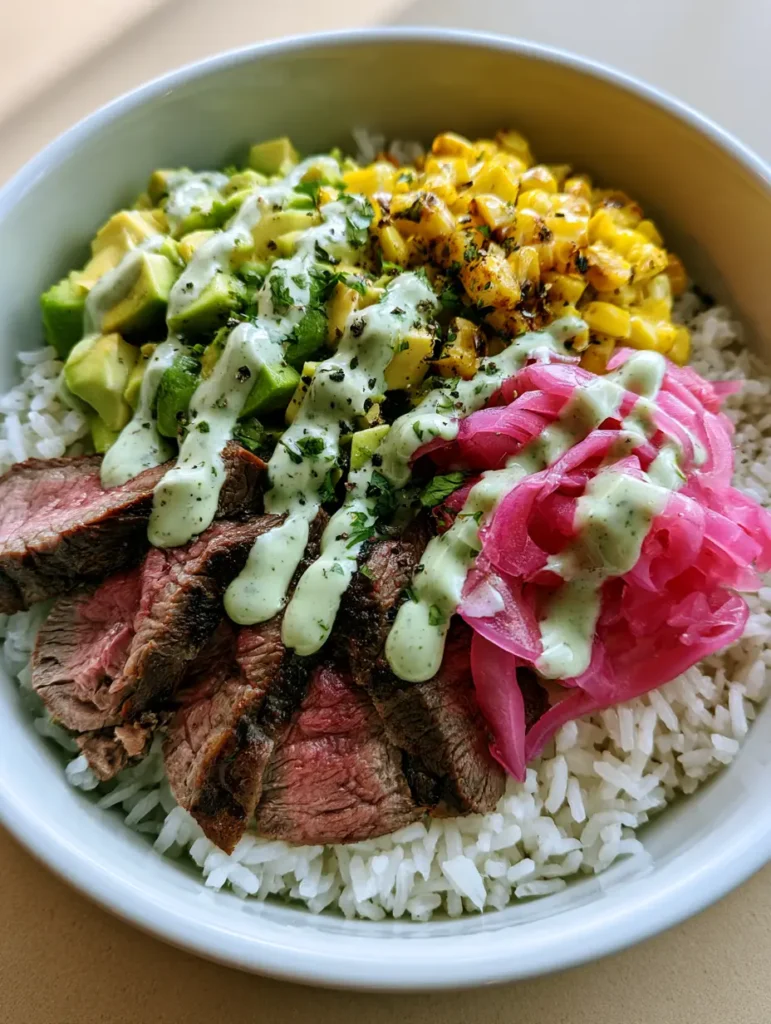 Steak and Avocado Bowl with Charred Corn and Cilantro Cream 2 Overhead view of a Steak and Avocado Bowl showing thick slices of medium-rare beef, bright pink onions, and a thick green sauce drizzle on white ceramic. (Steak and Avocado Bowl)