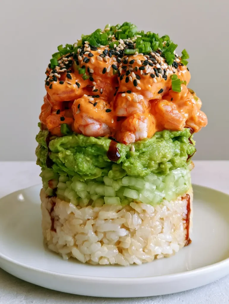 Cylindrical sushi stacks garnished with black and white sesame seeds and scallions on a minimalist gray background.