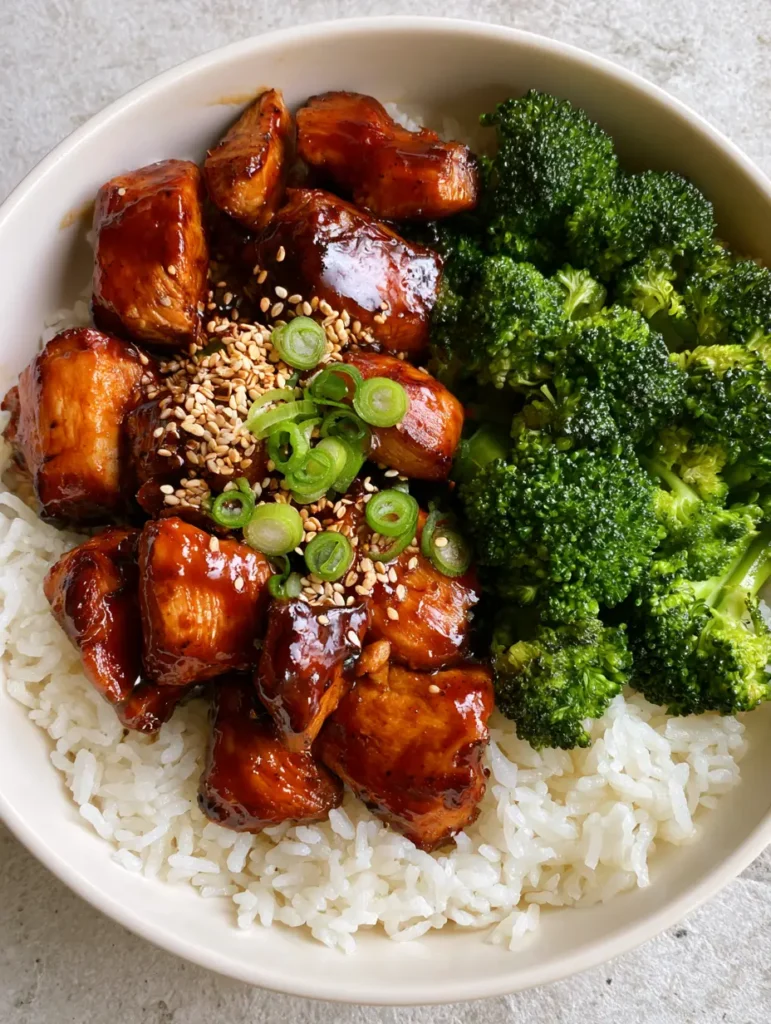 Teriyaki Chicken Bowl with Glossy Amber Glaze and Steamed Broccoli 1 A white ceramic bowl with individual jasmine rice grains, vibrant broccoli, and sesame garnished chicken. (Teriyaki Chicken Bowl)