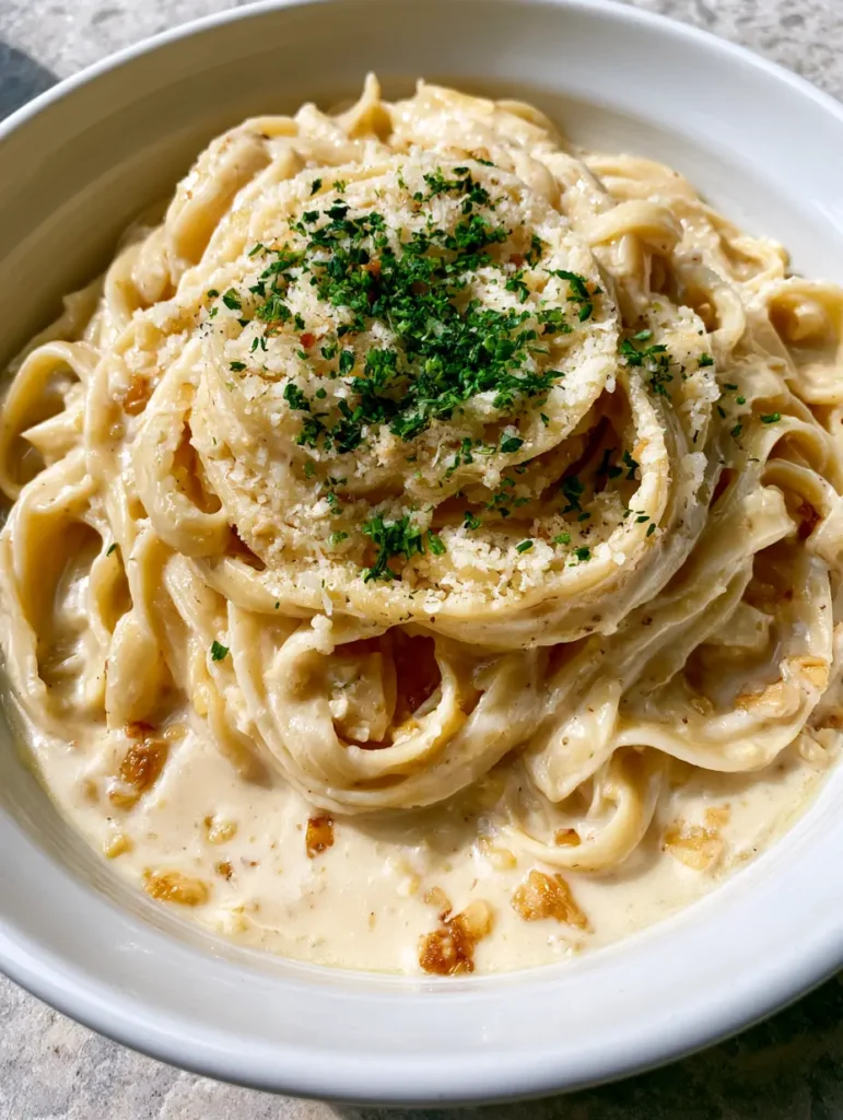 Overhead handheld shot of One Pot Creamy Garlic Pasta in a wide shallow white bowl showing glossy ivory sauce.