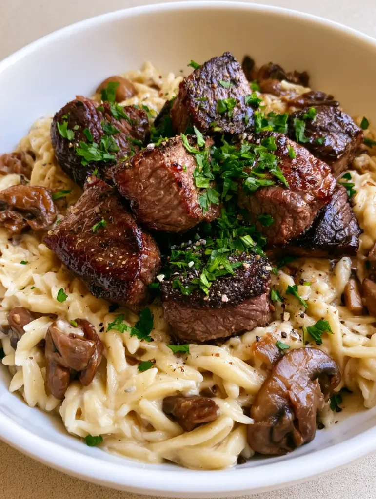 Steak Bites with Mushroom Orzo: A Creamy, One-Pan Steakhouse Masterpiece 2 Close-up view of seared steak bites showing a glistening caramelized crust on top of creamy orzo. (Steak Bites with Mushroom Orzo)