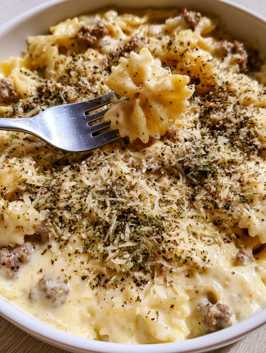 Close up of glossy garlic parmesan cream sauce on bowtie pasta with beef crumbles. (Creamy Parmesan Garlic Beef Bowtie Pasta)